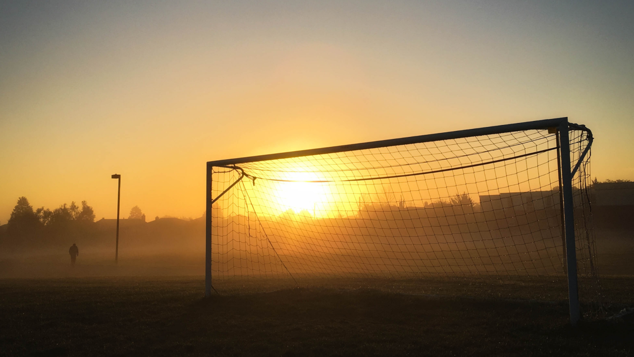 Soccer goal net bathed in golden light at sunset.