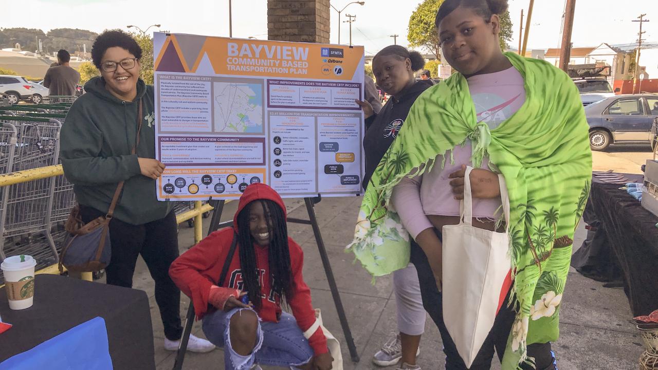 Four young people gather around a poster at a San Francisco Municipal Transit Authority community event