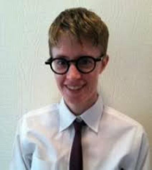 Kathleen Frederickson wearing a white button-down shirt and dark tie with glasses on.