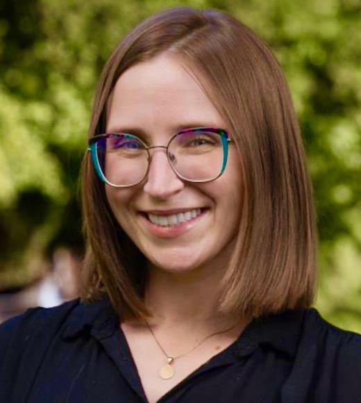 Smiling woman with shoulder-length hair and colorful glasses against a blurred green background.