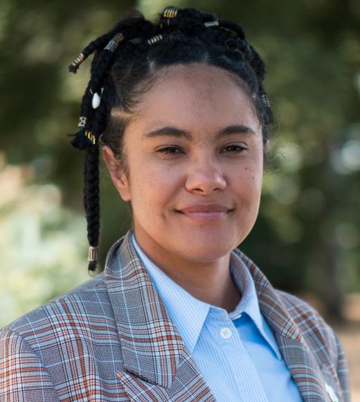 Portrait photo of a smiling person with beaded braids and plaid blazer