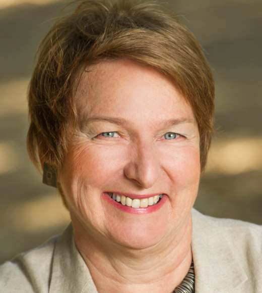 Smiling woman with short brown hair, wearing a light blazer, outdoors with a blurred background.
