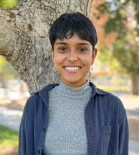 Medium shot of Ruchika Jaiswal in front of tree, wearing gray sweater and blue overshirt