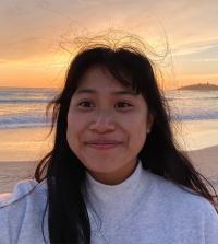 Head shot of Madeline Do against glowing backdrop of beach and ocean during golden hour