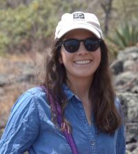 Portrait of Tara Pozzi, medium close up, in sunny outdoors, wearing blue shirt, sunglasses, and white cap
