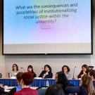 Photo: audience view of panelists beneath slide that reads, "What are the consequences and possibilities of institutionalizing social justice within the university?"