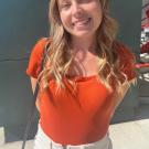Photo of Ellie Legg, medium shot in sunshine, wearing dark orange top