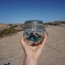 A photo of a hand holding onto a jar filled with plastic off a coast.