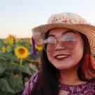 Portrait of Roella, wearing a hat, against a field of sunflowers