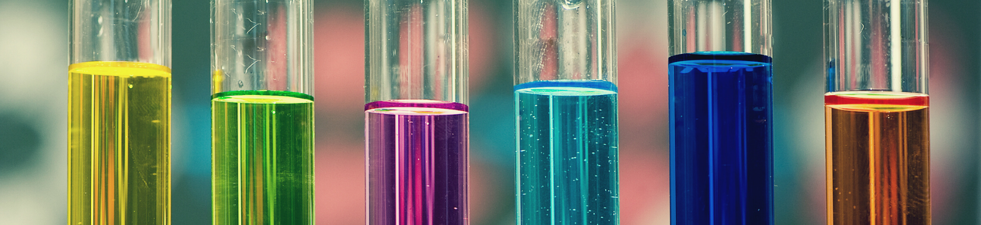 Six test tubes filled with six different colors of liquid: from left to right, yellow, green, purple, turquoise, blue, orange